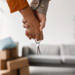 La foto ritrae una coppia che si tiene per mano e che stringe contemporaneamente un mazzo di chiavi. Nello sfondo si vedono degli scatoloni e un divano