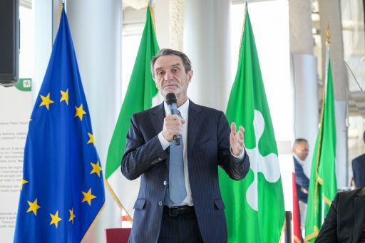 Il presidente Fontana con il microfono durante il suo intervento. Nello sfondo le bandiere dell'UE, dell'Italia e della Lombardia