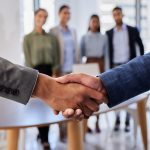 Stretta di mano in primo piano, dietro quattro persone sfumate: l’impegno di Legacoop Lombardia