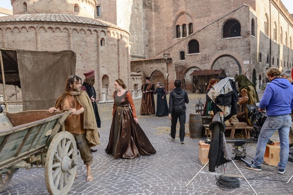Una scena di un film storico ambientato a Mantova. Sono presenti personaggi con abiti tradizionali e a destra ci sono degli operatori cinematografici