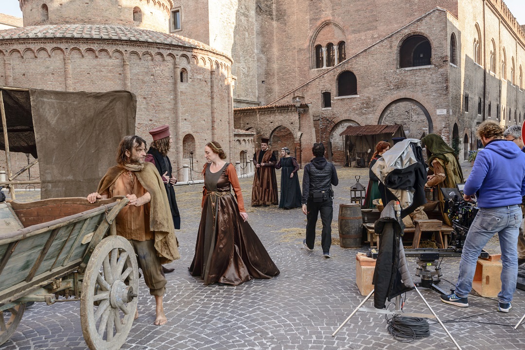 Una scena di un film storico ambientato a Mantova. Sono presenti personaggi con abiti tradizionali e a destra ci sono degli operatori cinematografici
