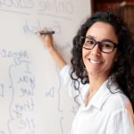 Una giovane insegnante mentre scrive su una lavagna bianca regole di grammatica. Foto utilizzata per l'articolo sul rientro dei giovani talenti dall'estero