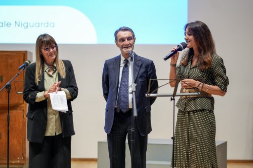L'assessore Lucchini con il microfono in mano mentre interviene. Presenti anche il presidente Fontana con la moderatrice sul palco dell'Auditorium Testori.