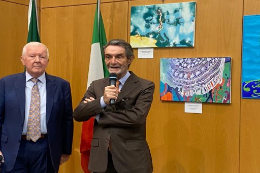 Il Presidente Attilio Fontana alla Mostra di street art Ricoh durante il suo intervento a Palazzo Lombardia. Ha in mano il microfono e sullo sfondo le bandiere e alcune opere. 