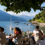 Una foto di Como vista lago, con i turisti seduti ad ammirare la bellezza lacustre: anche sulle sponde del Lario sono in programma numerosi eventi in Lombardia ad agosto