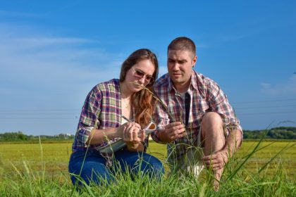una ragazza e un ragazzo giovani agronomi prendono nota su un quaderno dei dati relativi al terreno agricolo che stanno analizzando