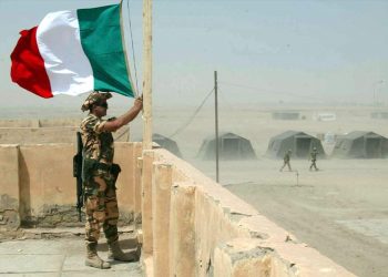 In foto un militare in servizio mentre sventola la bandiera italiana in memoria dei caduti di Nassiriya, onorati da Regione Lombardia con 14 borse di studio alle scuole
