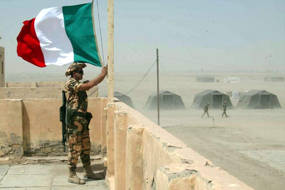 In foto un militare in servizio mentre sventola la bandiera italiana in memoria dei caduti di Nassiriya, onorati da Regione Lombardia con 14 borse di studio alle scuole