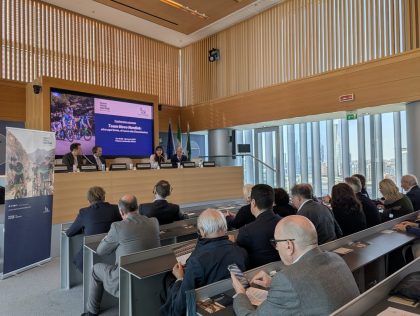 Conferenza a Palazzo Lombardia riguardo il Team Novo Nordisk Milano Sanremo. Panoramica della sala, l'assessore Lucchini sta facendo il suo intervento. Accanto a lei, seduti al tavolo altri ospiti. Dietro di loro la locandina della conferenza stampa.