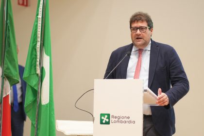 Assessore Giorgio Maione durante un suo intervento. E' in piedi dietro al logo di Regione Lombardia. Alla sua sinistra le bandiere dell'Italia e della Regione Lombardia. Foto utilizzata per Champions League’ delle idee