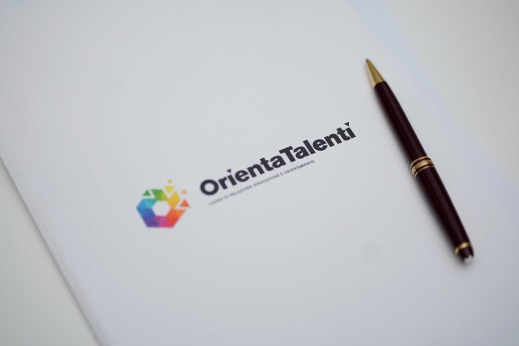 La foto mostra una cartellina con logo Orientatalenti 2026 con sopra appoggiata una penna. Foto scattata alla conferenza stampa di presentazione dell'evento che si terrà a Milano
