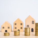 L'immagine mostra tre casette di legno in miniatura e cinque blocchi di monete che crescono progressivamente, a significare il prezzo degli affitti che cresce. Foto utilizzata per il contributo di Regione Lombardia per le famiglie con contratto d'affitto sul mercato libero