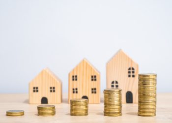 L'immagine mostra tre casette di legno in miniatura e cinque blocchi di monete che crescono progressivamente, a significare il prezzo dell'affitto che cresce. Foto utilizzata per il contributo di Regione Lombardia per le famiglie con contratto d'affitto sul mercato libero