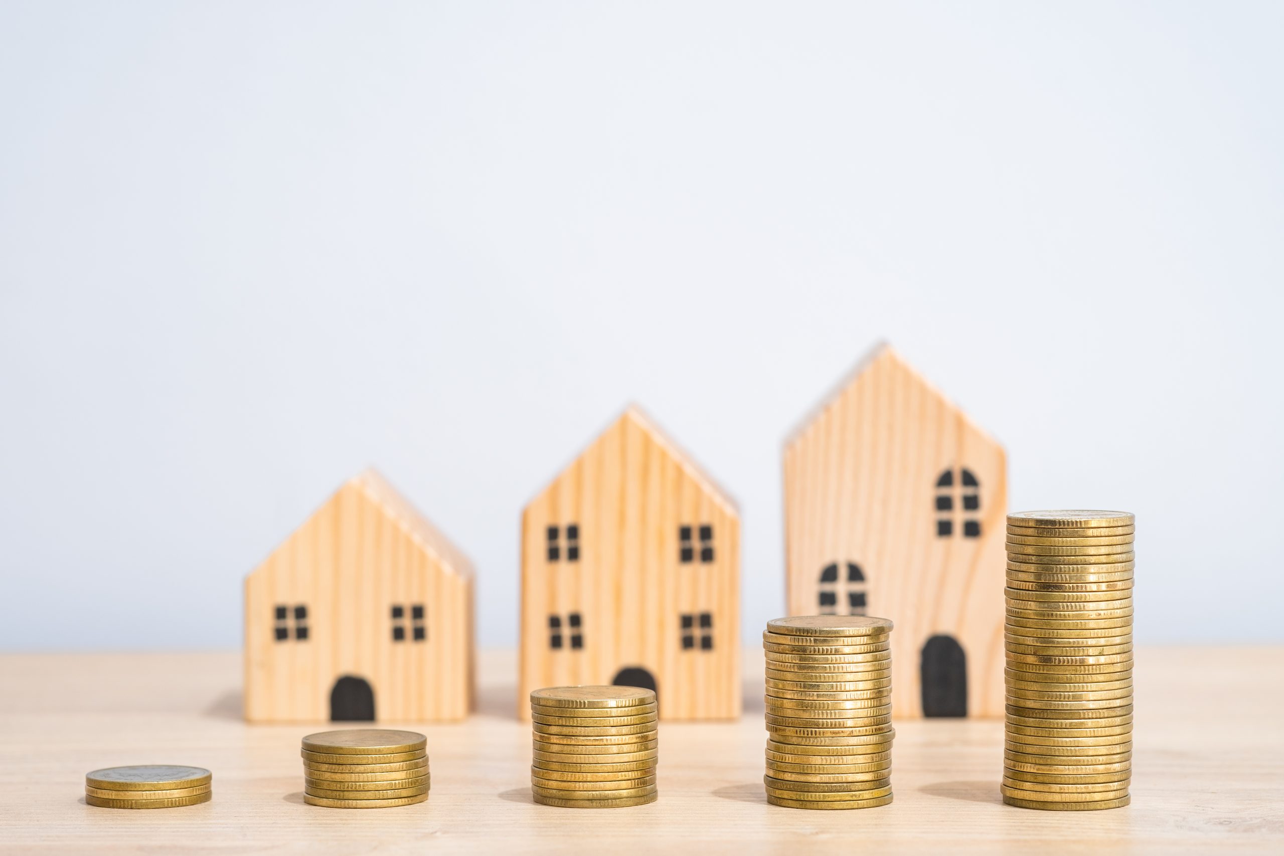 L'immagine mostra tre casette di legno in miniatura e cinque blocchi di monete che crescono progressivamente, a significare il prezzo dell'affitto che cresce. Foto utilizzata per il contributo di Regione Lombardia per le famiglie con contratto d'affitto sul mercato libero