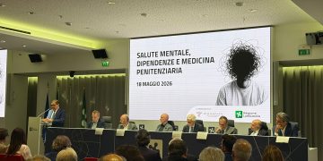 Convegno Associazione Ippocrate Salute mentale; l'immagine ritrae l'assessore La Russa durante il suo intervento; la visuale permette di vedere la locandina dell'evento trasmessa nel led e gli altri interlocutori seduti al tavolo.