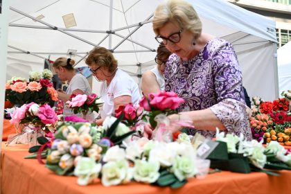 In foto un gruppo di signore dello stand dedicato ai fiori di carta di Monte Isola (Brescia) in posa in piazza Città di Lombardia in occasione della Festa della Regione 2026