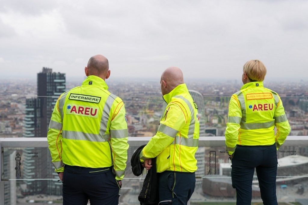 La foto mostra tre operatori di Areu ritratti di spalle mentre guardano la città di Milano. Immagine utilizzata per articolo medici della Lombardia partiti per il venezuela