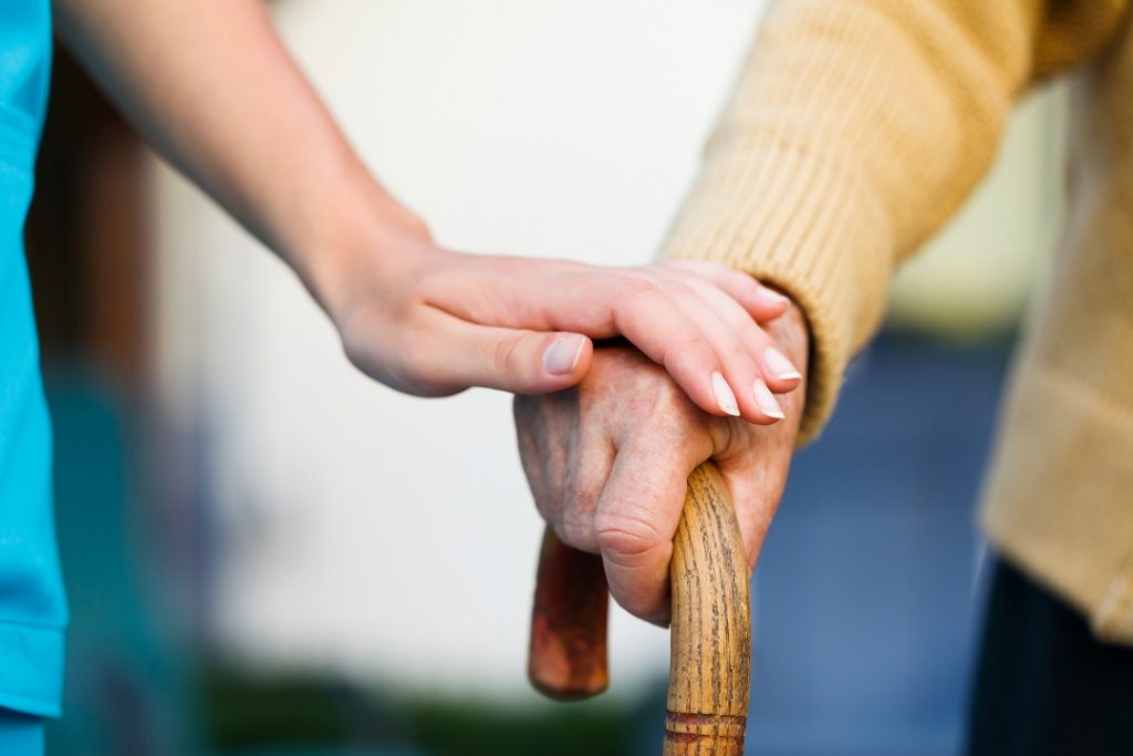 L'immagine ritrae una mano di un'anziano che si sorregge sul bastone e una mano di un'altra persona poggiata sopra. Immagine utilizzata per il Forum sostenibilità sociale che si è tenuto a Palazzo Lombardia