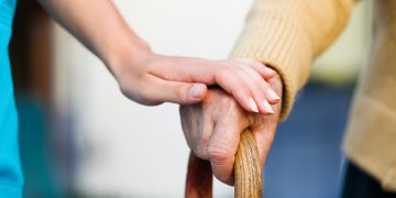 L'immagine ritrae una mano di un'anziano che si sorregge sul bastone e una mano di un'altra persona poggiata sopra. Immagine utilizzata per il Forum sostenibilità sociale che si è tenuto a Palazzo Lombardia