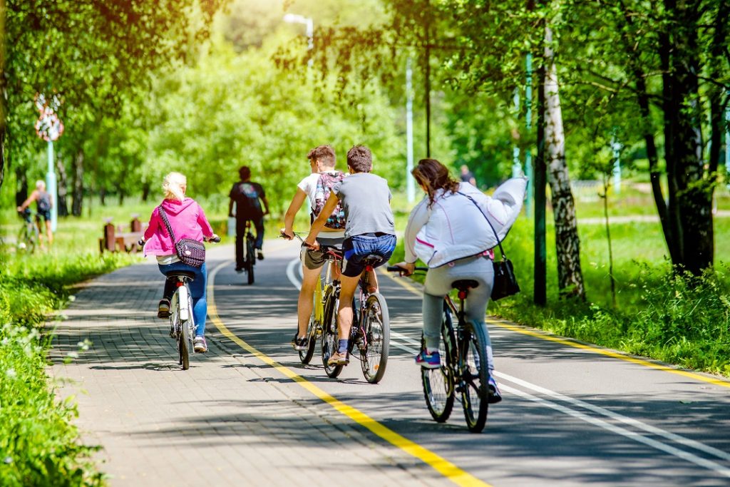 La foto mostra un gruppo di persone in bicicletta che attraversa una pista ciclabile immersa in un'area verde. Immagine utilizzata per l'articolo riguardante l'aggiornamento dell'elenco degli interventi finanziati dal Piano Lombardia: nuove piste ciclabili per Albiate (Monza Brianza) e Opera (Milano).