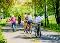 La foto mostra un gruppo di persone in bicicletta che attraversa una pista ciclabile immersa in un'area verde. Immagine utilizzata per l'articolo riguardante l'aggiornamento dell'elenco degli interventi finanziati dal Piano Lombardia: nuove piste ciclabili per Albiate (Monza Brianza) e Opera (Milano).