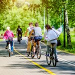 La foto mostra un gruppo di persone in bicicletta che attraversa una pista ciclabile immersa in un'area verde. Immagine utilizzata per l'articolo riguardante l'aggiornamento dell'elenco degli interventi finanziati dal Piano Lombardia: nuove piste ciclabili per Albiate e Milano