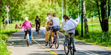 La foto mostra un gruppo di persone in bicicletta che attraversa una pista ciclabile immersa in un'area verde. Immagine utilizzata per l'articolo riguardante l'aggiornamento dell'elenco degli interventi finanziati dal Piano Lombardia: nuove piste ciclabili per Albiate (Monza Brianza) e Opera (Milano).