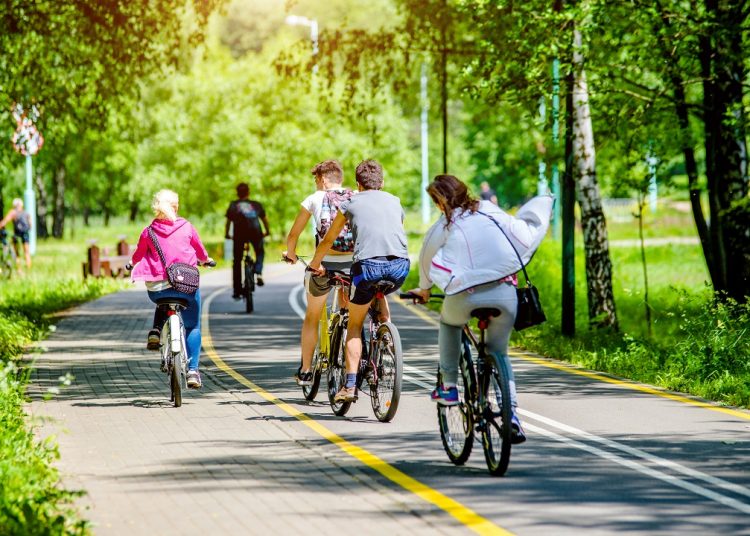 La foto mostra un gruppo di persone in bicicletta che attraversa una pista ciclabile immersa in un'area verde. Immagine utilizzata per l'articolo riguardante l'aggiornamento dell'elenco degli interventi finanziati dal Piano Lombardia: nuove piste ciclabili per Albiate (Monza Brianza) e Opera (Milano).
