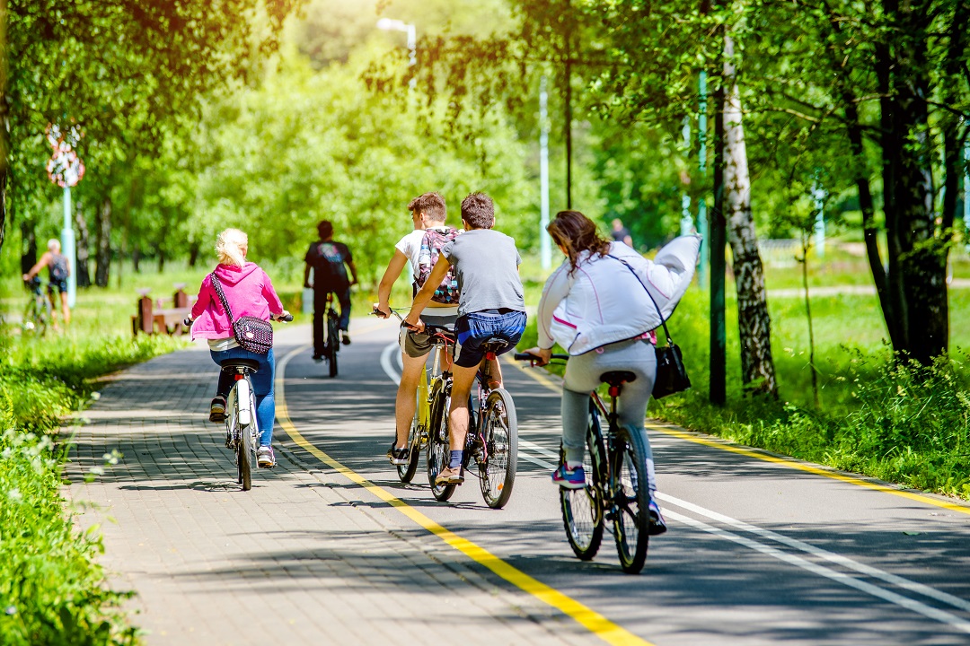 La foto mostra un gruppo di persone in bicicletta che attraversa una pista ciclabile immersa in un'area verde. Immagine utilizzata per l'articolo riguardante l'aggiornamento dell'elenco degli interventi finanziati dal Piano Lombardia: nuove piste ciclabili per Albiate (Monza Brianza) e Opera (Milano).