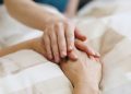 Tema fine vita, immagine utilizzata per il silenzio di Regione Lombardia nel caso del lombardo affetto di sclerosi multipla accompagnato alla morte. La foto mostra una mano appoggiata a due mani giunte di una persona che si trova su un letto di ospedale.
