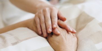 Tema fine vita, immagine utilizzata per il silenzio di Regione Lombardia nel caso del lombardo affetto di sclerosi multipla accompagnato alla morte. La foto mostra una mano appoggiata a due mani giunte di una persona che si trova su un letto di ospedale.