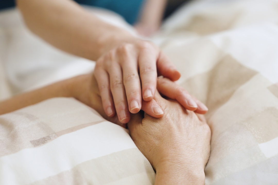 Tema fine vita, immagine utilizzata per il silenzio di Regione Lombardia nel caso del lombardo affetto di sclerosi multipla accompagnato alla morte. La foto mostra una mano appoggiata a due mani giunte di una persona che si trova su un letto di ospedale.