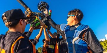 L'immagine mostra alcuni giovani di una squadra di baseball che festeggiano una vittoria alzando le mazze e i caschi