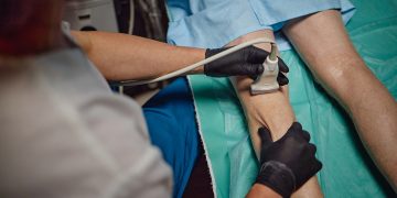 Uomo riceve esame ecografico vascolare sulla parte inferiore della gamba da un medico che indossa guanti in ambiente clinico. Immagine utilizzata per Rete regionale della Chirurgia Vascolare di Regione Lombardia.