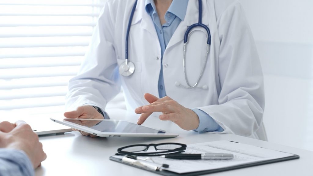 Cambiano i tempi di validità delle ricette in Lombardia. La foto mostra un medico che prescrive una ricetta con il tablet. Si trova sulla sua scrivania difronte al paziente