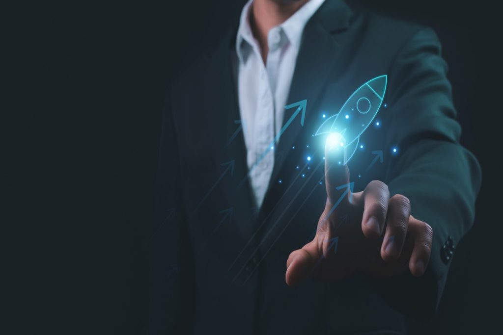 L'immagine mostra un uomo in abito da lavoro nello sfondo e in primo piano una mano che 'clicca' su un razzo grafico, dando l'idea di dare un'accelerata alla sua azienda. Utilizzata per il progetto Pianeta Accelerator per le startup di Regione Lombardia