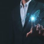 L'immagine mostra un uomo in abito da lavoro nello sfondo e in primo piano una mano che 'clicca' su un razzo grafico, dando l'idea di dare un'accelerata alla sua azienda. Utilizzata per illustrare la presentazione del progetto Pianeta Accelerator per le startup di Regione Lombardia