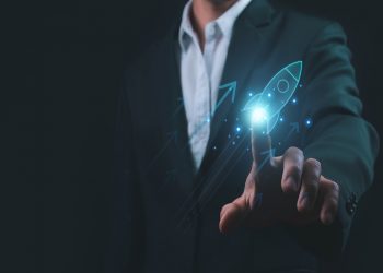 L'immagine mostra un uomo in abito da lavoro nello sfondo e in primo piano una mano che 'clicca' su un razzo grafico, dando l'idea di dare un'accelerata alla sua azienda. Utilizzata per illustrare la presentazione del progetto Pianeta Accelerator per le startup di Regione Lombardia