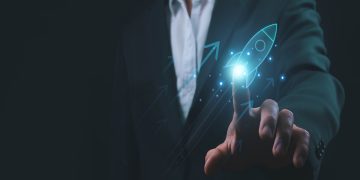 L'immagine mostra un uomo in abito da lavoro nello sfondo e in primo piano una mano che 'clicca' su un razzo grafico, dando l'idea di dare un'accelerata alla sua azienda. Utilizzata per illustrare la presentazione del progetto Pianeta Accelerator per le startup di Regione Lombardia