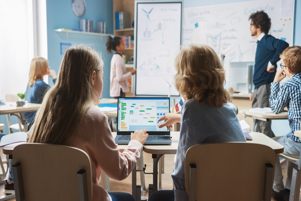 Studenti a scuola di spalle che guardano un computer. Immagine utilizzata per primo giorno di scuola, con messaggio del presidente Fontana